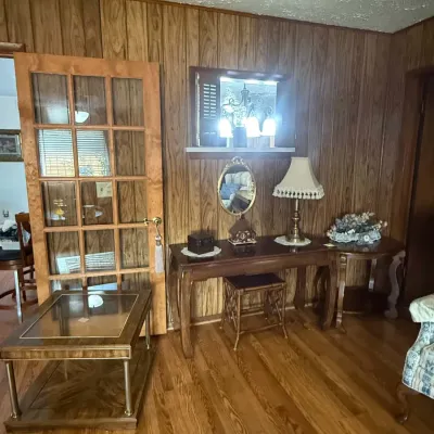 Mid-century wood-paneled room featuring a wooden vanity table with matching stool, a glass-top end table, and a 15-pane glass door.