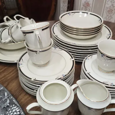 Vintage fine china dinnerware set featuring a delicate floral motif, black and gold trim, and matching serving pieces including a creamer...