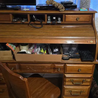 Vintage oak rolltop desk with matching wooden chair, featuring multiple drawers, cubby organizers, and brass hardware.