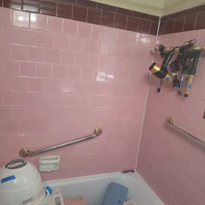 Assorted bathroom items, including a Conair facial sauna, hair styling tools, towels, and a bath mat, displayed in a vintage pink-tiled...