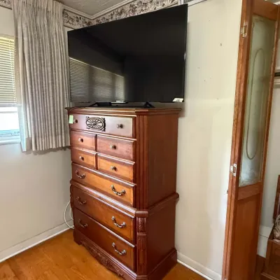 Traditional cherry wood tallboy chest of drawers featuring ornate carved details and brass hardware, shown supporting a flat-screen...