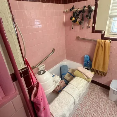 Vintage mid-century bathroom featuring pink and maroon wall tiles, pink mosaic floor tiles, and various bath linens and hair styling...