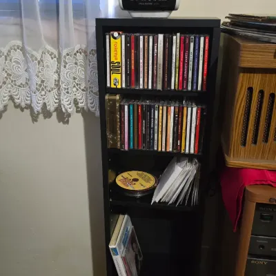 Tall black wooden CD tower filled with various music CDs, topped with a vintage Sony Dream Machine clock radio.