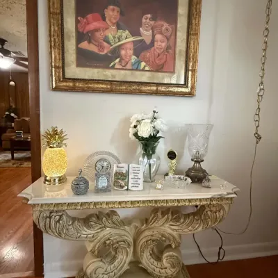 Ornate neoclassical-style console table with a marble top and heavily carved scroll base, displaying various decorative items including a...