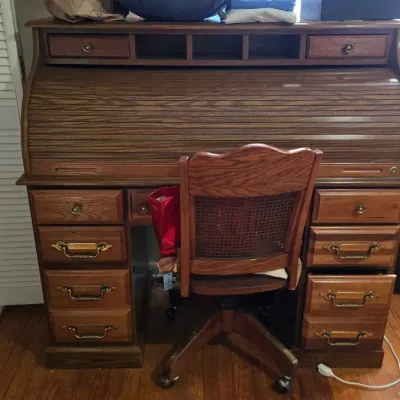 Vintage oak rolltop desk with matching cane-back swivel office chair, featuring multiple drawers and brass hardware.