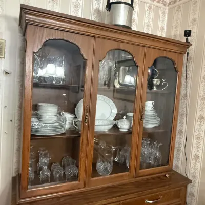Vintage oak china cabinet with arched glass doors, filled with various glassware, crystal, and fine china sets.