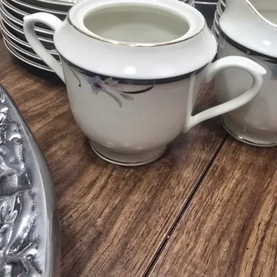 Vintage fine china sugar bowl and creamer set with a delicate floral and silver band design, shown alongside matching plates and saucers.