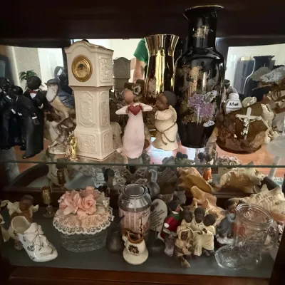A collection of vintage figurines, vases, and decorative collectibles displayed inside a wooden curio cabinet with glass shelves.