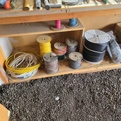 Sale Photo Thumbnail #48: Assorted spools of electrical wire and cable in various gauges and colors, stored on a wooden workbench shelf.
