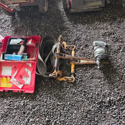 Sale Photo Thumbnail #40: Assorted heavy-duty tools including a red Hilti storage case with accessories, a coiled tow strap, a yellow chain binder, and a vintage corded power drill.