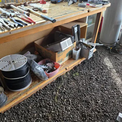 Sale Photo Thumbnail #49: Wooden workbench with various hand tools, hardware, and a spool of black strapping tape stored on the lower shelf.