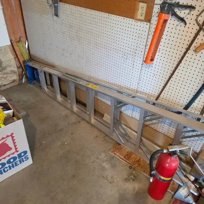 Sale Photo Thumbnail #61: Werner aluminum extension ladder shown collapsed and resting on a garage floor next to a pegboard wall.