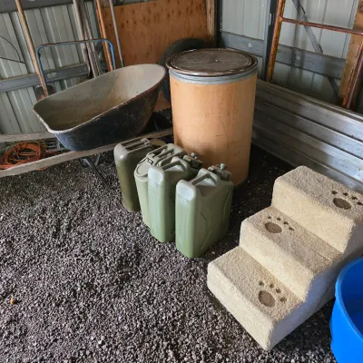 Sale Photo Thumbnail #37: Assorted utility items including a wheelbarrow, a fiber drum, three olive drab jerry cans, and a carpeted three-step pet stair with paw print details.
