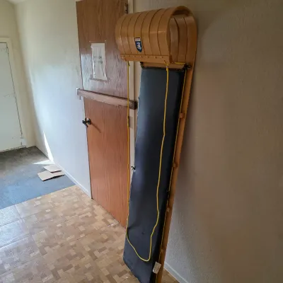 Sale Photo Thumbnail #14: Vintage wooden toboggan sled with a black padded cushion and yellow pull rope, leaning against a wall.