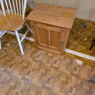 Sale Photo Thumbnail #13: Oak icebox-style end table with a single cabinet door and brass-finished hardware, shown next to a white wooden Windsor-style chair.