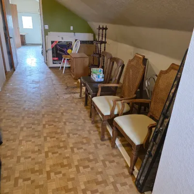 Sale Photo Thumbnail #7: Assorted vintage dining and accent chairs, including a pair of cane-back armchairs with light upholstery, lined up in an attic hallway.