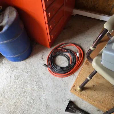 Sale Photo Thumbnail #93: Coiled heavy-duty extension cords in orange and black, resting on a concrete floor next to a red metal tool cabinet.