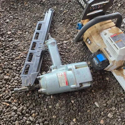Sale Photo Thumbnail #47: Pneumatic framing nailer and a Hart brushless battery-powered chainsaw resting on gravel.