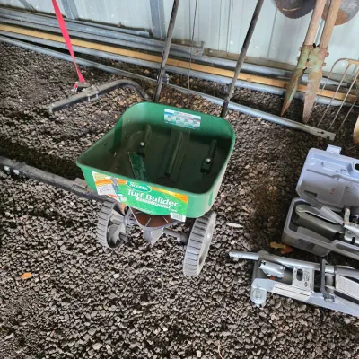 Sale Photo Thumbnail #57: Scotts Turf Builder EdgeGuard Mini walk-behind lawn spreader, shown alongside a hydraulic floor jack and other garage tools.