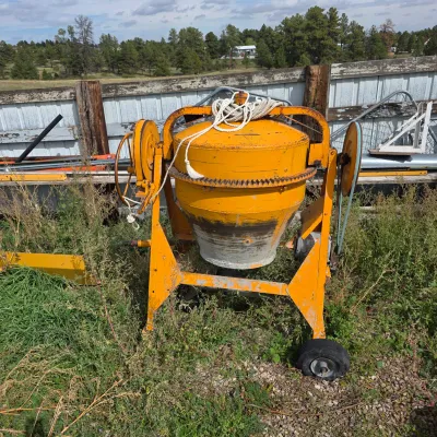 Sale Photo Thumbnail #77: Vintage yellow portable cement mixer on wheels, showing some wear and rust from outdoor use.