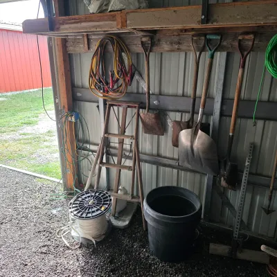 Sale Photo Thumbnail #39: Assorted garage and garden tools, including a wooden stepladder, various shovels, a black plastic bucket, jumper cables, and a spool of wire.