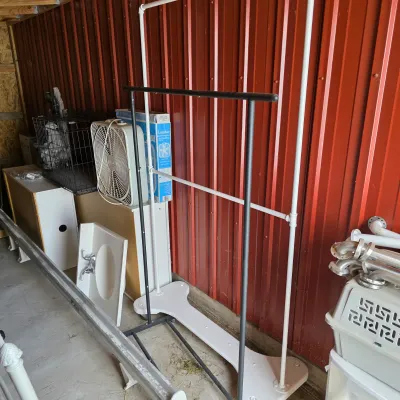 Sale Photo Thumbnail #94: Assorted household and utility items, including a black metal garment rack, a white PVC frame, a Lasko box fan, and a wire pet crate, stored in a shed.