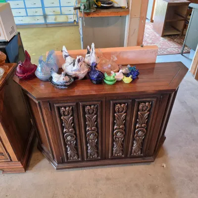 Sale Photo Thumbnail #72: Vintage dark wood credenza with ornate carved door panels, displaying a collection of colorful glass hen-on-nest covered dishes.