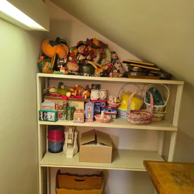 Sale Photo Thumbnail #21: White metal shelving unit holding an assortment of seasonal decorations, including Easter baskets, Thanksgiving plush items, decorative tins, and craft supplies.