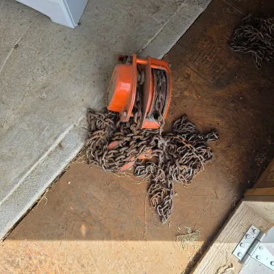 Sale Photo Thumbnail #85: Vintage orange manual chain hoist with rusted heavy-duty lifting chain, showing signs of wear and outdoor storage.