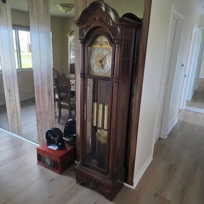 Sale Photo Thumbnail #2: Vintage grandfather clock featuring an ornate carved wooden case, a decorative brass dial with Roman numerals, and visible brass weights and pendulum.