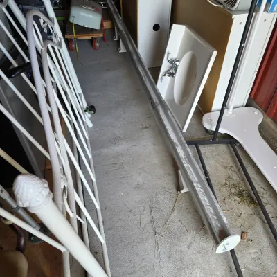 Sale Photo Thumbnail #95: Assorted household and building materials, including a white metal headboard, a long metal track, and a white bathroom sink basin with faucet.
