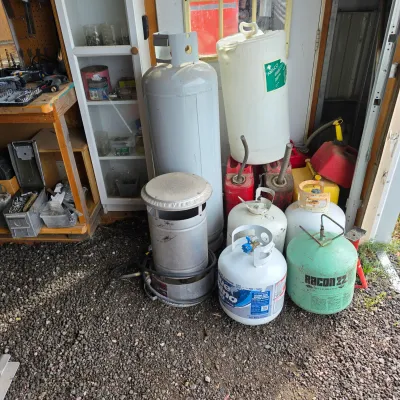 Sale Photo Thumbnail #24: Assorted propane tanks, gas cans, and a portable heater stored outdoors on a gravel surface.