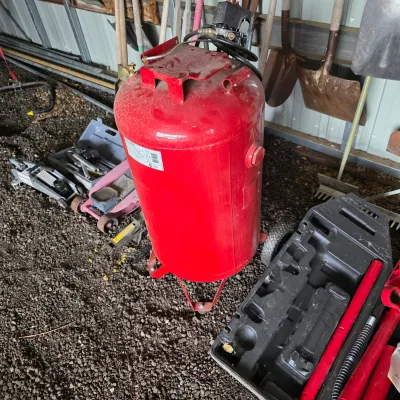 Sale Photo Thumbnail #30: Large red vertical air compressor tank shown in a garage setting alongside various automotive jacks and hand tools.
