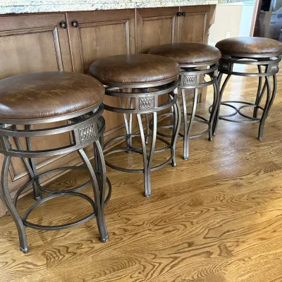 Set of four modern swivel counter stools featuring metal frames with decorative aprons and round brown faux-leather cushioned seats.