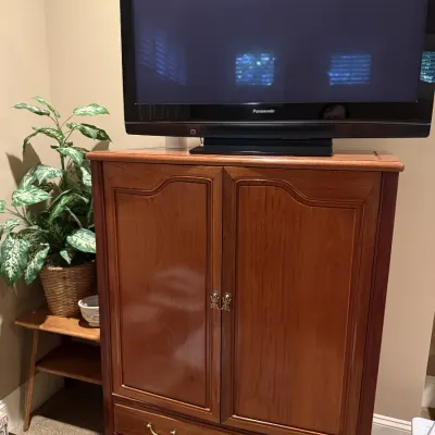 Traditional wooden media armoire cabinet with brass hardware, featuring double doors and lower drawers, topped with a Panasonic...
