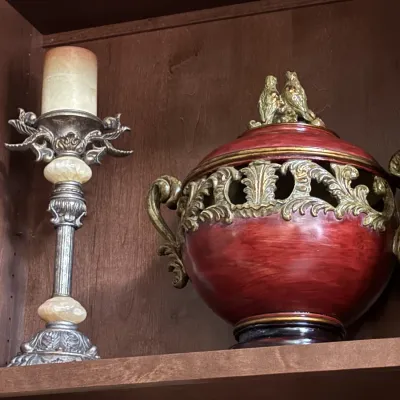 Ornate silver-toned candlestick with a pillar candle, paired with a red glaze ceramic urn featuring gold scrollwork details and a bird...