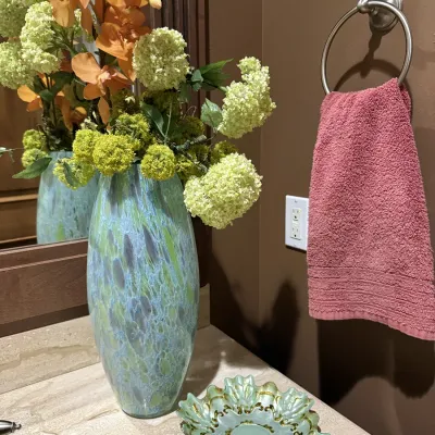 Tall art glass vase with mottled blue and green finish, holding artificial hydrangeas and orchids, paired with a matching decorative...