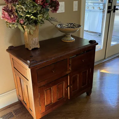 Rustic wood server featuring two upper drawers and two panel doors, topped with a faux floral arrangement and a decorative ceramic...