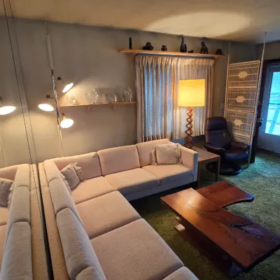 Mid-century modern living room featuring a large beige sectional sofa, a live-edge wood coffee table, a tension pole lamp, and a vintage...