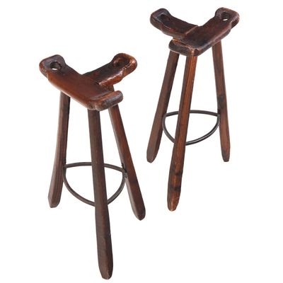 A PAIR OF FRENCH CARVED WOOD TRIPOD SADDLE STOOLS HAVING IRON FOOT RESTS.