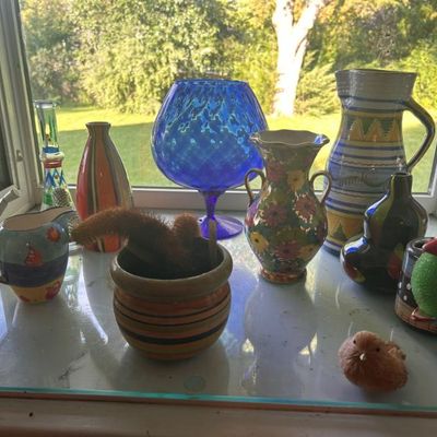 Sale Photo Thumbnail #43: Collection of colorful decorative glassware and ceramics, including a large blue glass goblet, floral and striped vases, and a small potted cactus.