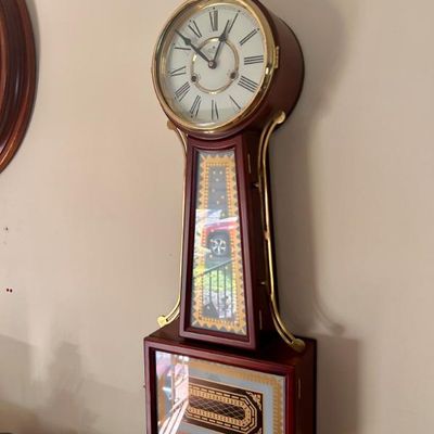 Sale Photo Thumbnail #58: Vintage banjo wall clock featuring a mahogany-finished wooden case, brass side brackets, and decorative reverse-painted glass panels.