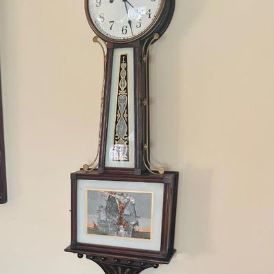 Sale Photo Thumbnail #15: Antique New Haven banjo wall clock featuring a wooden case with brass side brackets and a painted lower glass panel depicting a sailing ship.