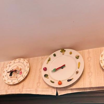 Sale Photo Thumbnail #41: Collection of novelty wall clocks fashioned from decorative ceramic plates, including three with illustrated scenes and one featuring three-dimensional vegetable markers with fork and knife hands.
