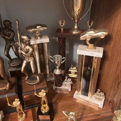 Sale Photo Thumbnail #114: Collection of vintage sports and racing trophies, featuring baseball players, race cars, and classic cup designs.