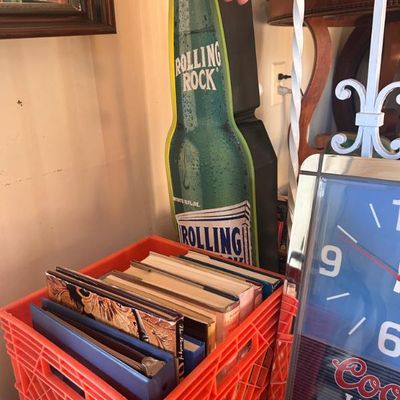 Sale Photo Thumbnail #28: Vintage Rolling Rock beer bottle-shaped advertising sign alongside a crate of books and a Coors Light clock.