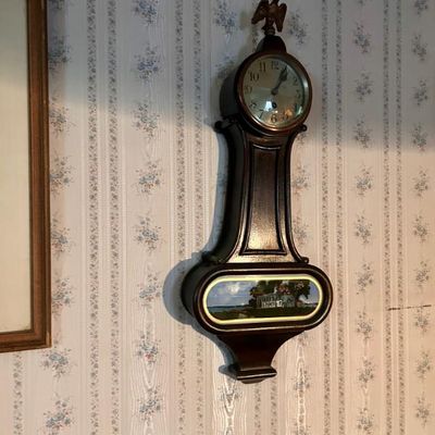 Sale Photo Thumbnail #38: Vintage banjo wall clock featuring a dark wood case, an eagle finial, and a painted lower glass panel depicting a scenic landscape.