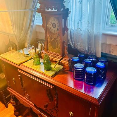 Sale Photo Thumbnail #37: Antique wooden parlor clock, green onyx desk sets, and cobalt blue glassware displayed on a vintage wooden sideboard.