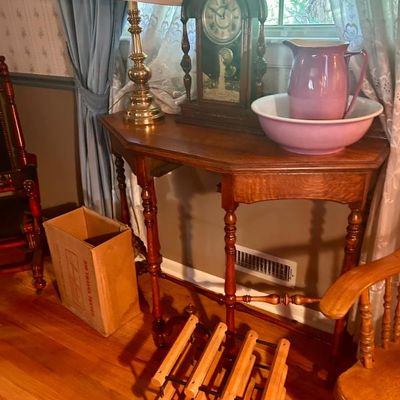 Sale Photo Thumbnail #47: Antique wooden console table with turned legs, featuring a brass table lamp, a vintage mantel clock, and a purple ceramic pitcher and basin set.