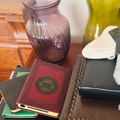 Sale Photo Thumbnail #85: Assorted vintage items including a purple ribbed glass vase, an olive green glass vase, a small red leather-bound book with a Federal Deposit Insurance Corporation seal, and a brown studded leather box.